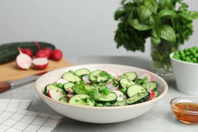 Photo of Appetizing salad with cucumbers, radish and pea in bowl served on light grey table