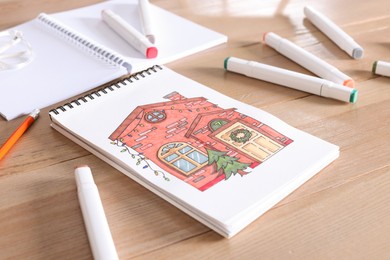 Photo of Sketchbook with beautiful drawing of house and felt tip pens on wooden table