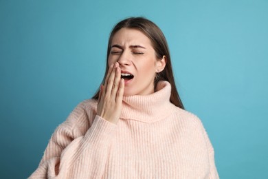 Young tired woman yawning on light blue background