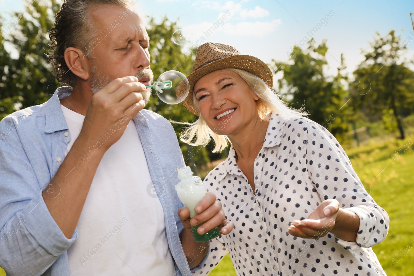 Photo of Lovely mature couple spending time together in park. Man blowing soap bubbles