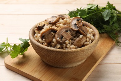 Delicious pearl barley with mushrooms, parsley and dill on wooden table, closeup