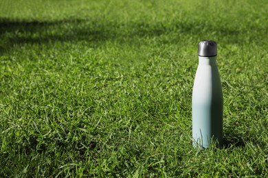Photo of Thermo bottle on green grass in park, space for text