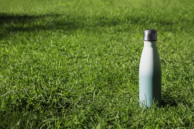 Thermo bottle on green grass in park, space for text