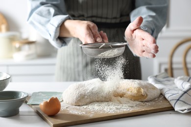 Photo of Making dough. Woman sifting flour at white wooden table in kitchen, closeup