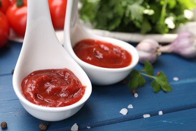 Photo of Organic ketchup in spoons and spices on blue wooden table, closeup. Tomato sauce