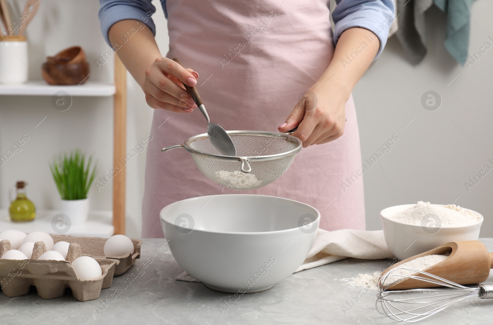 Photo of Making tasty baklava. Woman sifting flour into bowl at light grey marble table, closeup