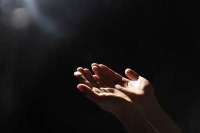 Religion. Woman with open palms praying on black background, closeup. Space for text