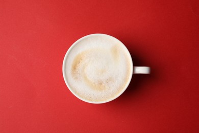 Photo of Tasty cappuccino in coffee cup on red background, top view