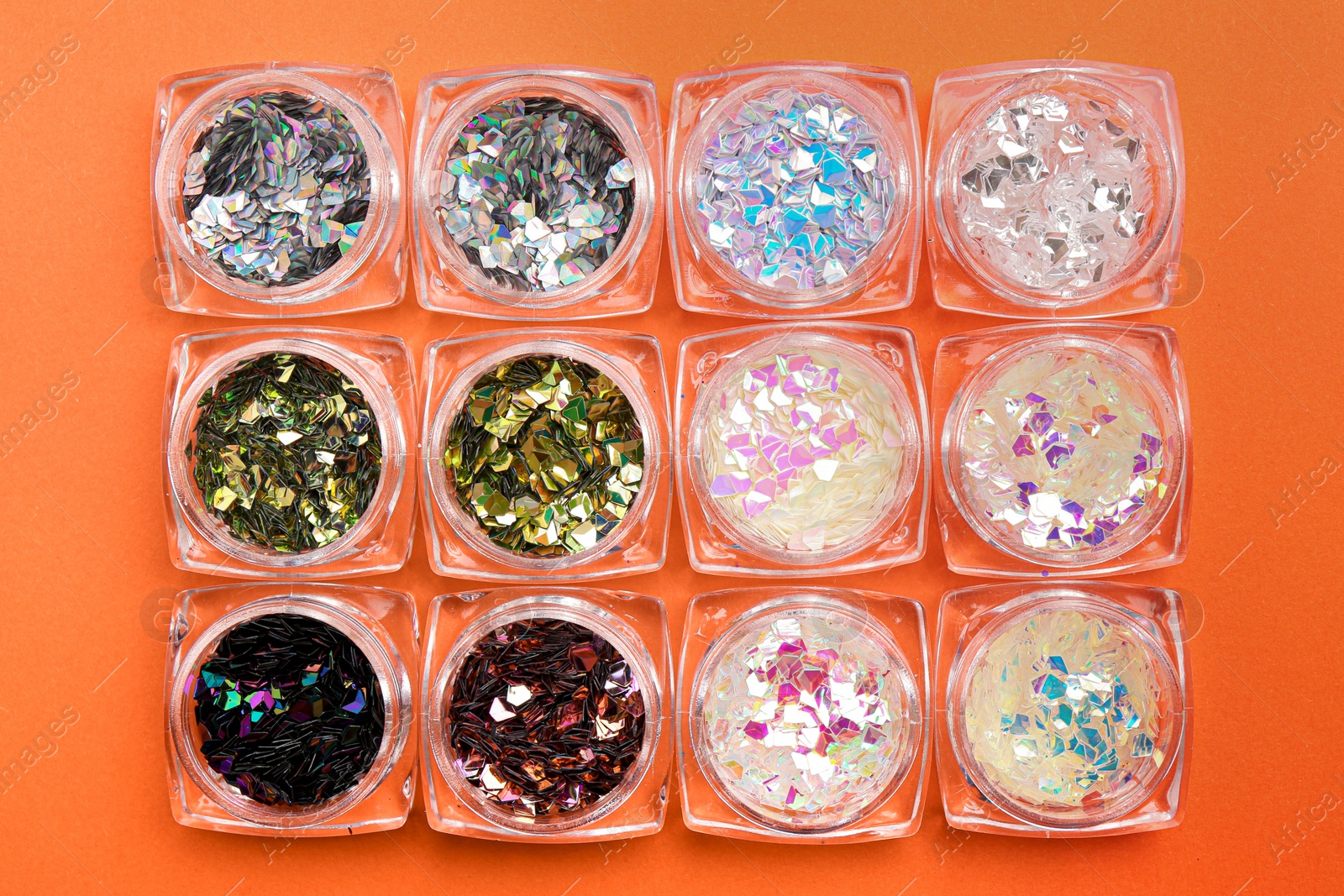 Photo of Jars with colorful shiny glitter on orange background, flat lay