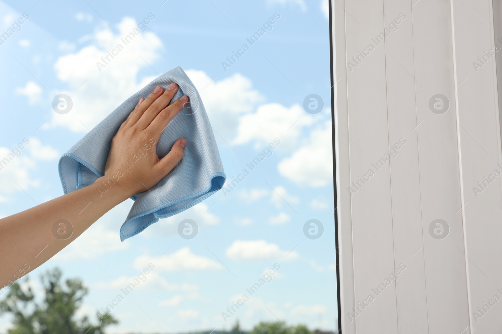 Photo of Woman cleaning window glass with rag indoors, closeup