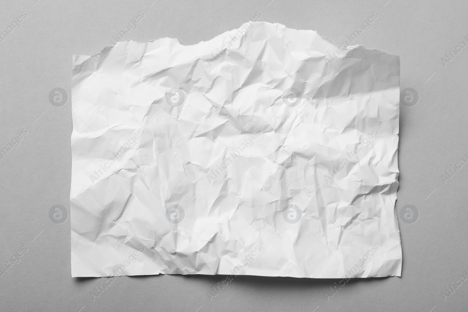 Photo of Sheet of white crumpled paper on grey background, top view