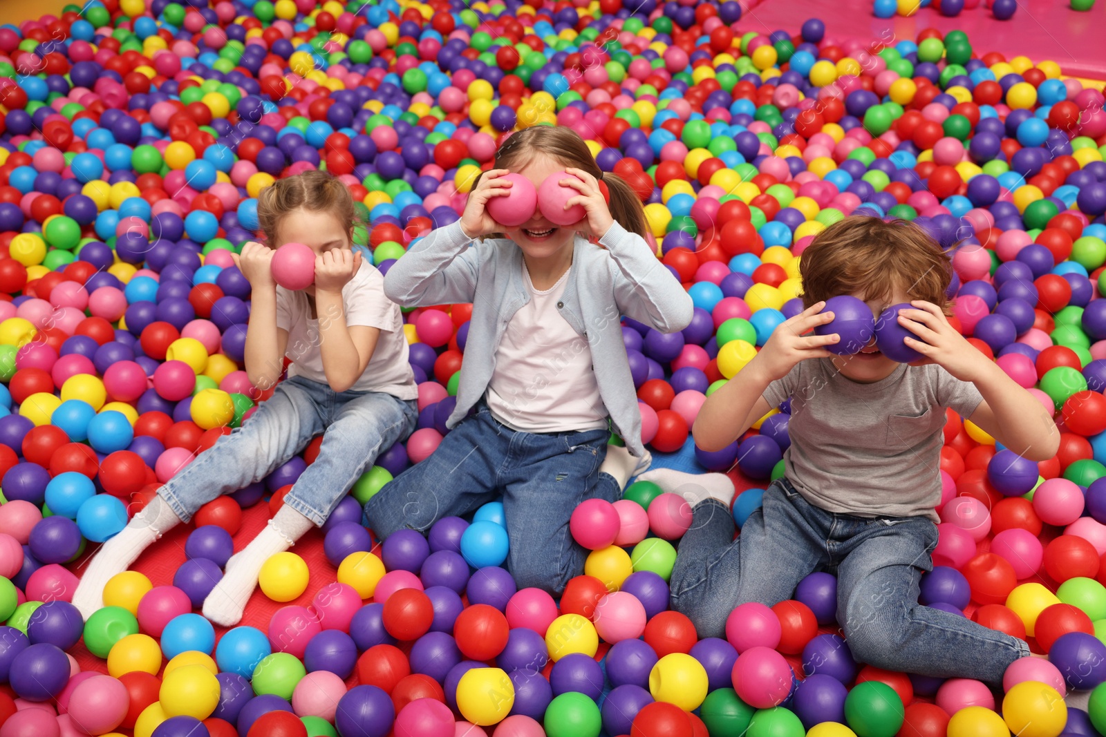 Photo of Happy little kids sitting on colorful balls in ball pit