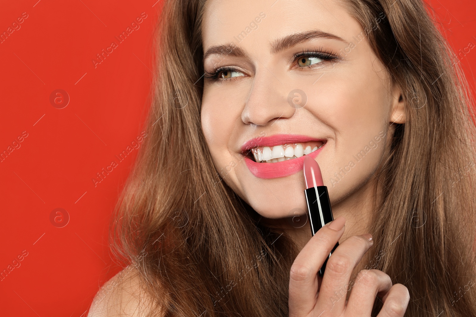 Photo of Young woman applying beautiful lipstick on color background
