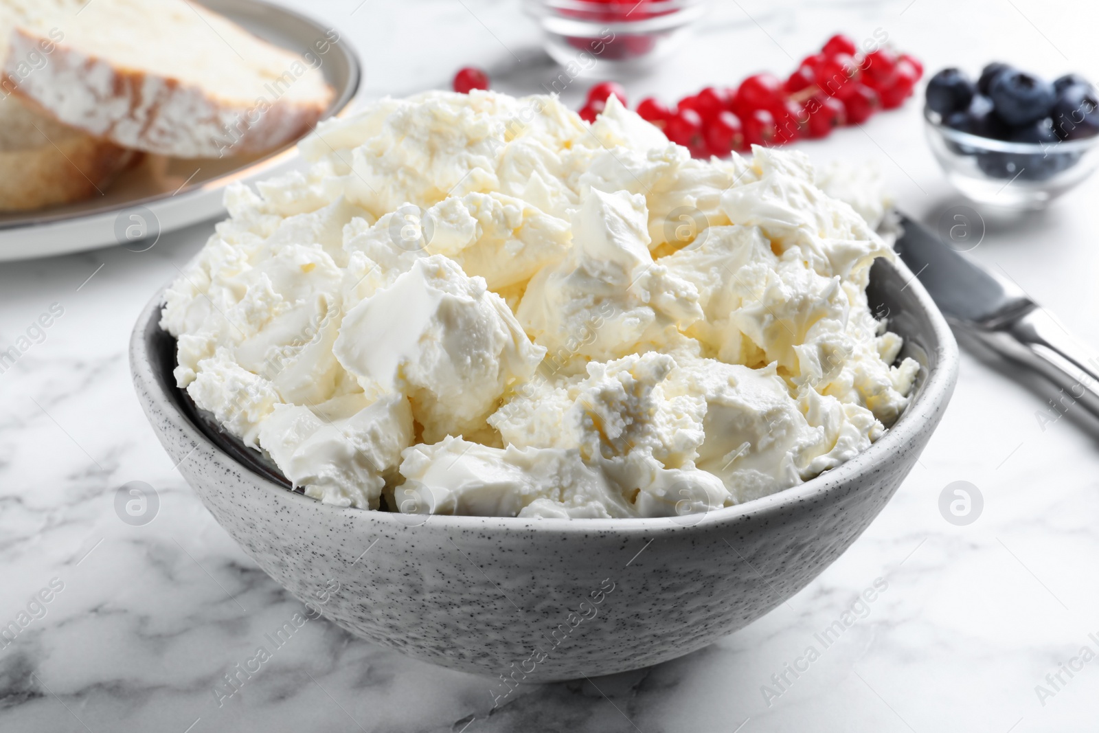 Photo of Tasty cream cheese and fresh berries on white marble table