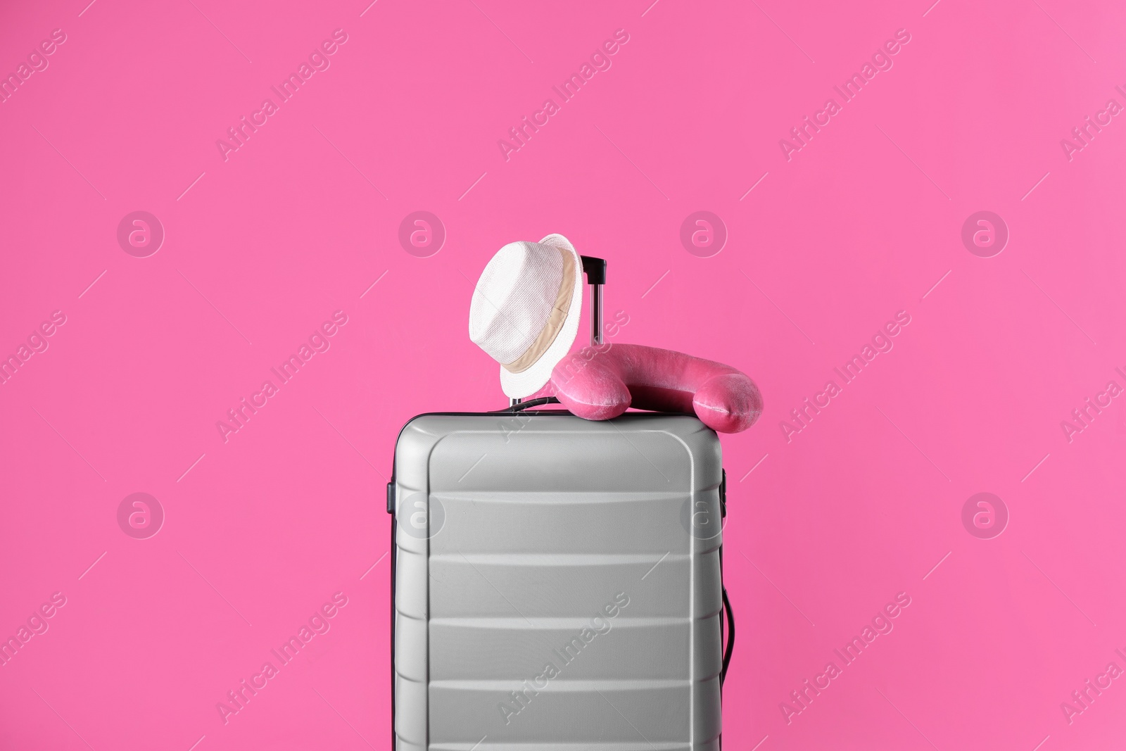 Photo of Grey suitcase, hat and travel pillow on pink background