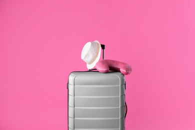 Photo of Grey suitcase, hat and travel pillow on pink background