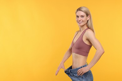 Photo of Slim woman wearing big jeans on yellow background, space for text. Weight loss