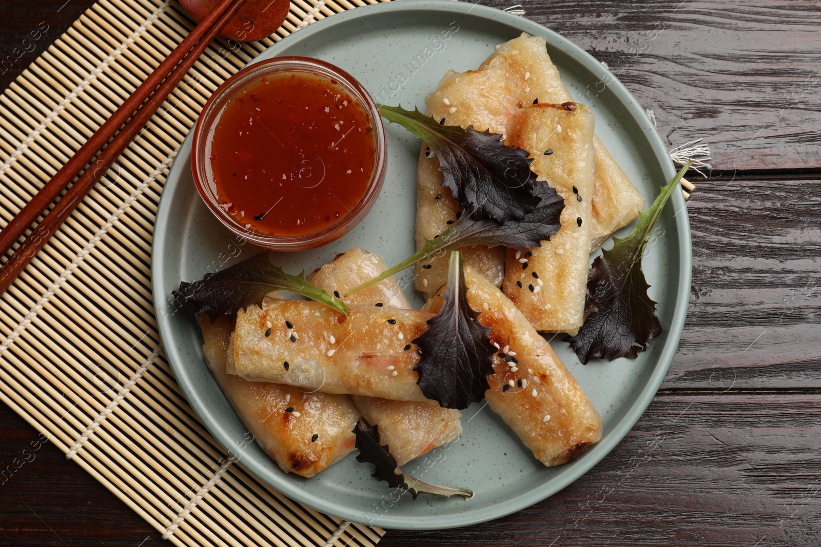 Photo of Tasty fried spring rolls, lettuce and sauce on wooden table, top view