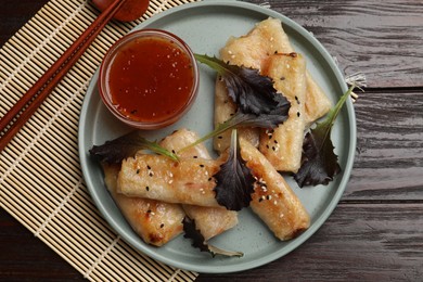 Photo of Tasty fried spring rolls, lettuce and sauce on wooden table, top view