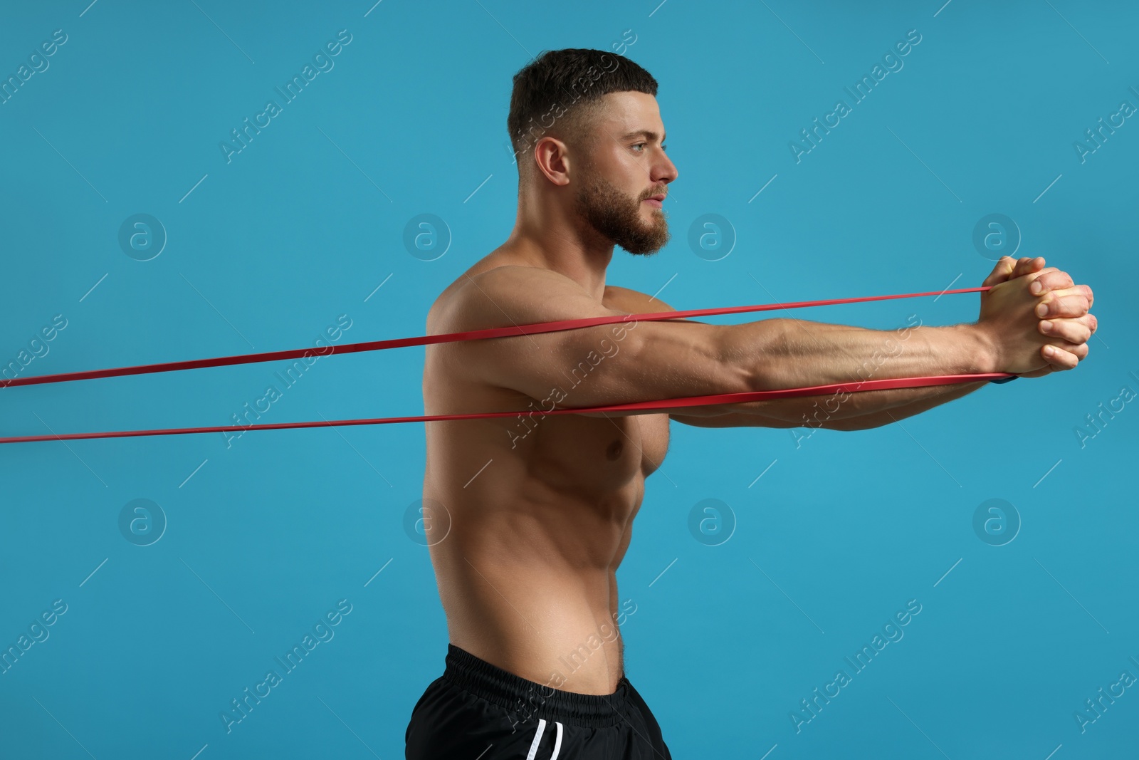 Photo of Muscular man exercising with elastic resistance band on light blue background