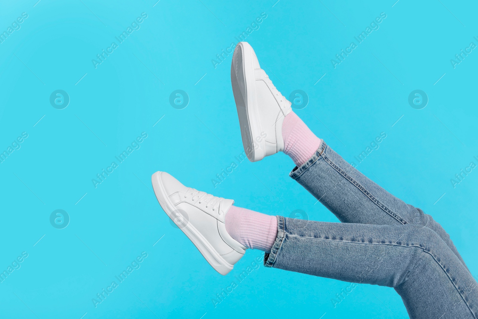 Photo of Woman wearing stylish white sneakers on light blue background, closeup