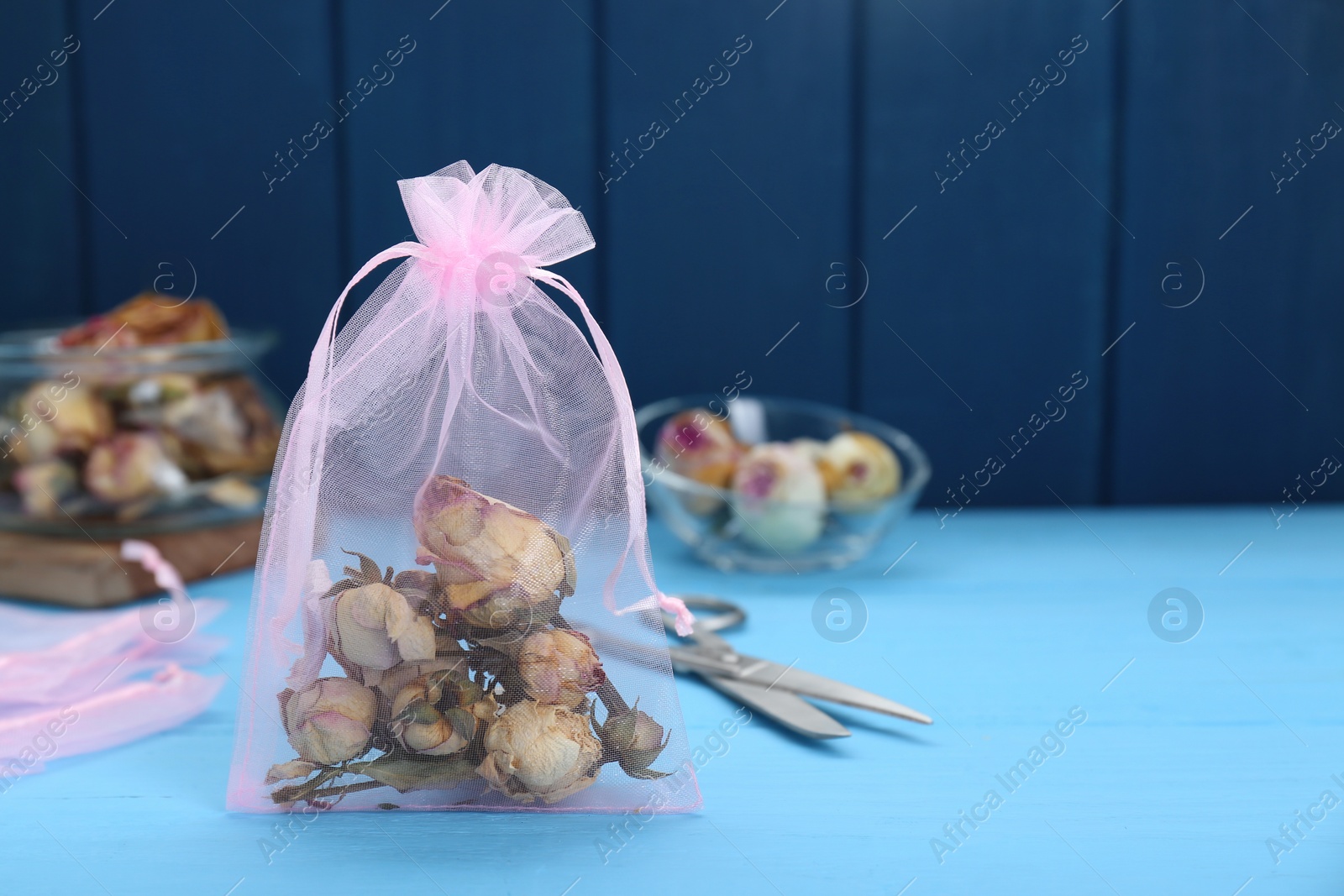 Photo of Scented sachet with dried roses on light blue table, space for text