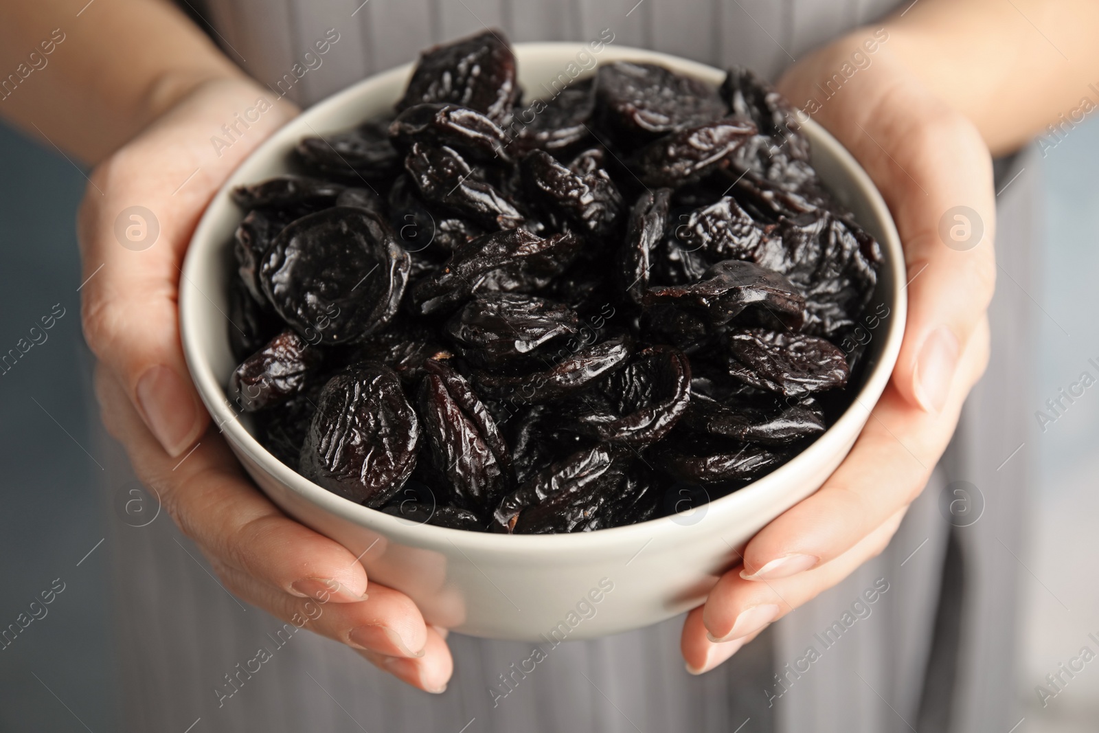 Photo of Woman holding bowl of dried plums, closeup. Healthy fruit