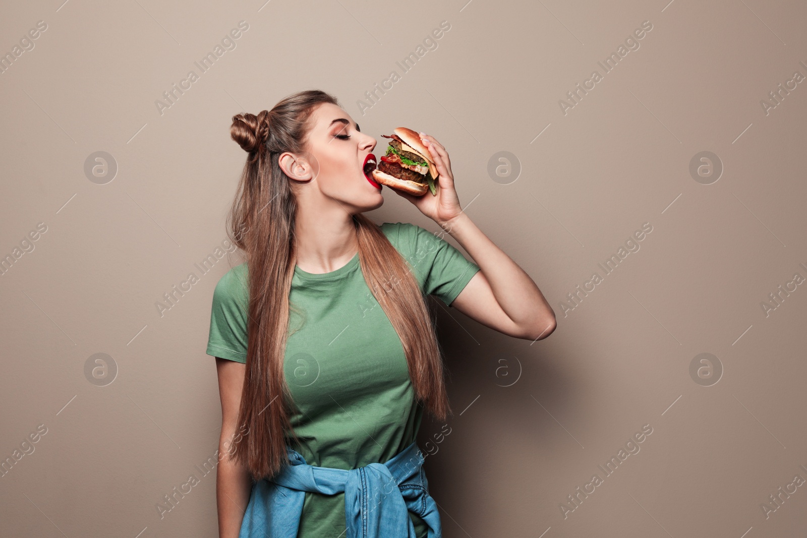 Photo of Pretty woman eating tasty burger on color background. Space for text