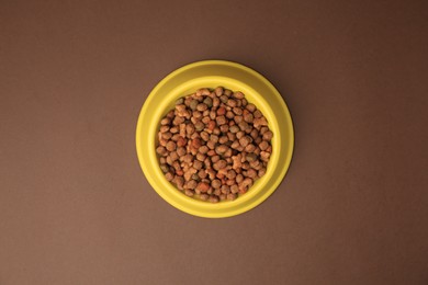 Photo of Dry pet food in feeding bowl on brown background, top view