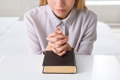 Photo of Religious young woman with Bible praying at home, closeup
