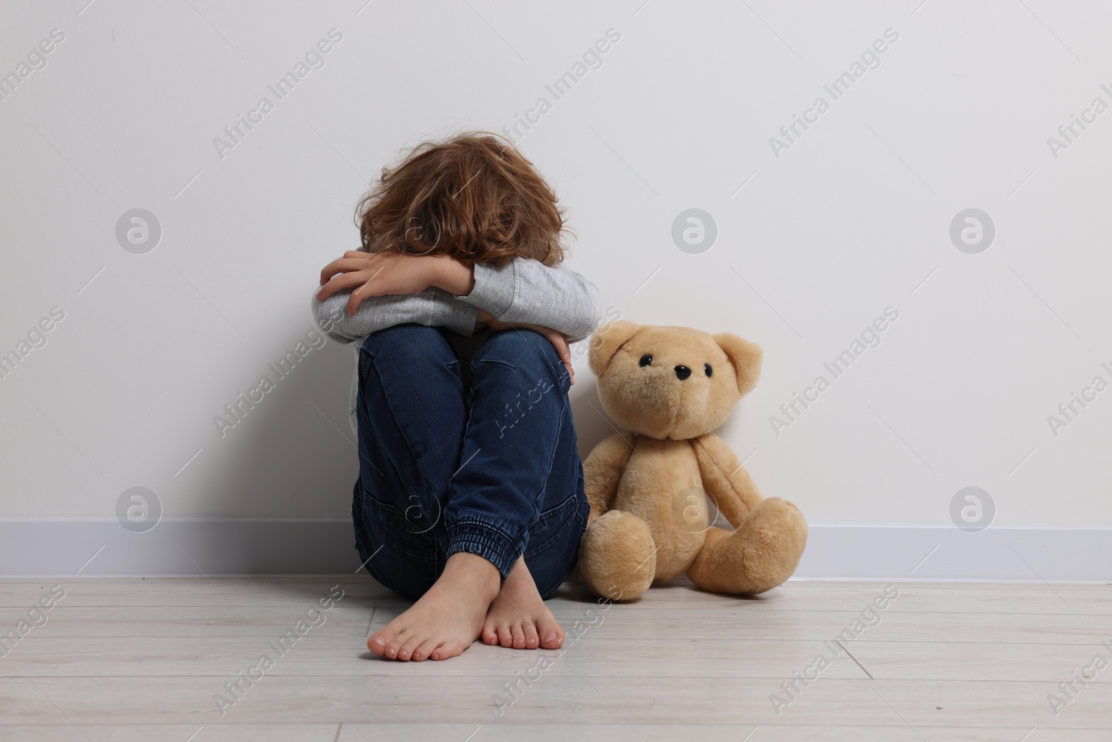 Photo of Child abuse. Upset boy with toy sitting on floor near white wall