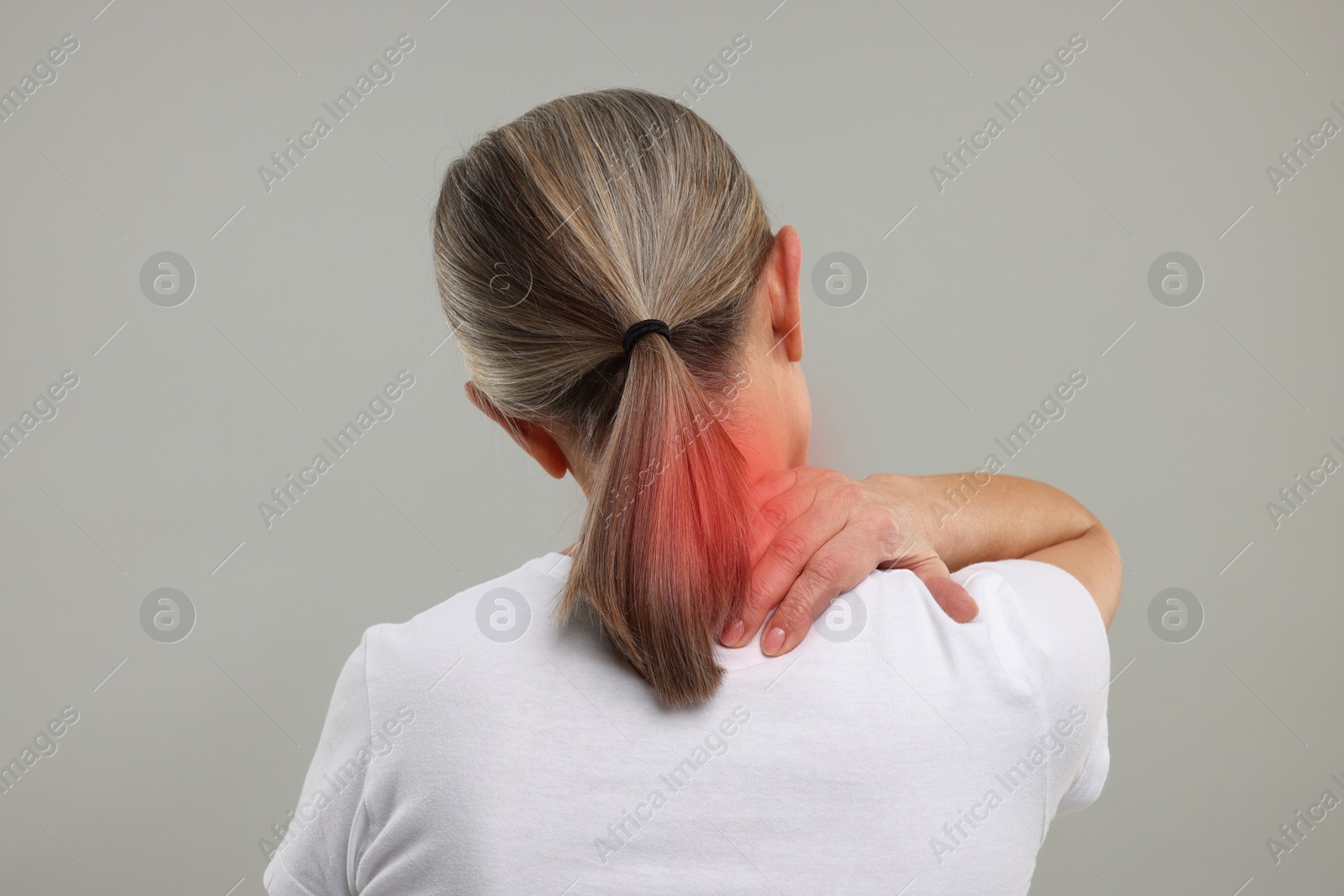 Image of Woman suffering from neck pain on grey background, back view