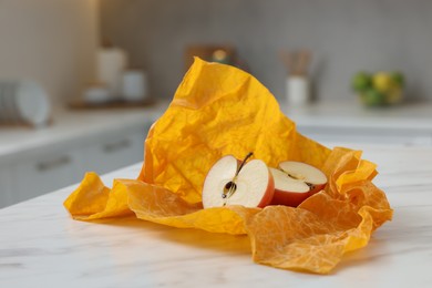 Photo of Halves of apple with orange beeswax food wrap on white table, closeup