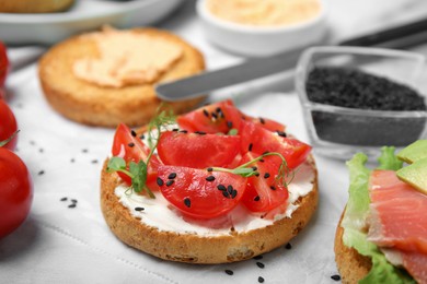 Photo of Tasty rusk with cream cheese, fresh tomatoes and black sesame seeds on white table, closeup