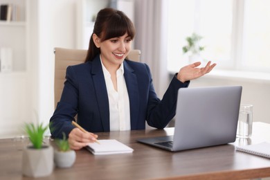 Photo of Woman taking notes during webinar at wooden table indoors