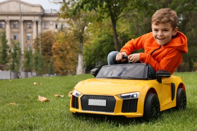 Photo of Cute little boy driving children's car in park. Space for text