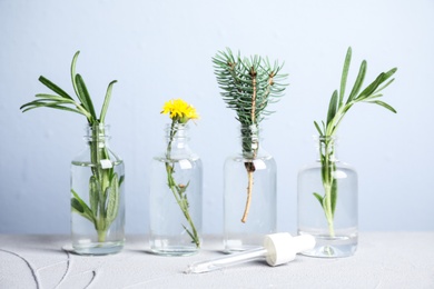 Photo of Glass bottles of different essential oils with plants on table