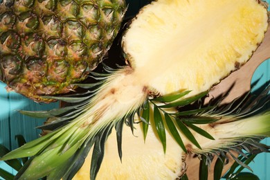 Whole and cut ripe pineapples on light blue wooden table, flat lay