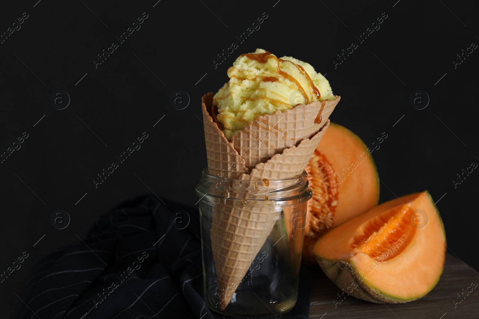 Photo of Delicious melon ice cream in wafer cone and glass jar on table, closeup