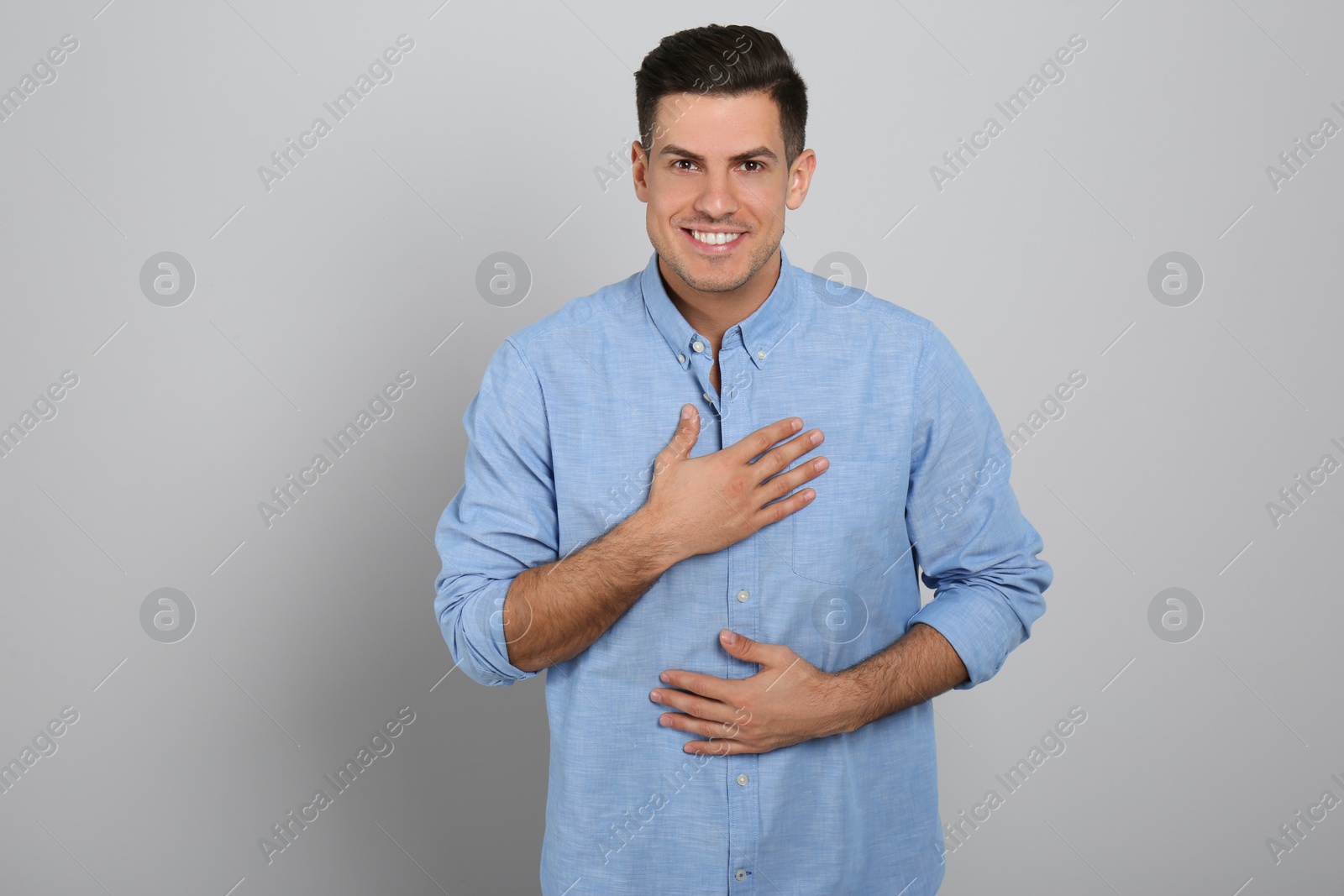 Photo of Handsome grateful man with hands on chest against light grey background
