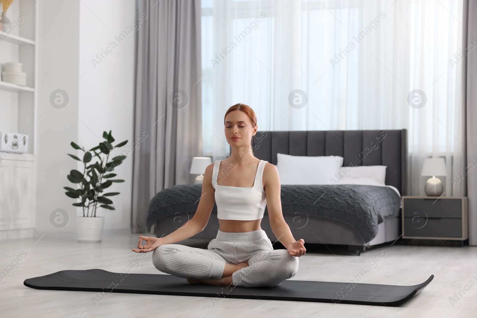 Photo of Beautiful young woman practicing Padmasana on yoga mat at home. Lotus pose