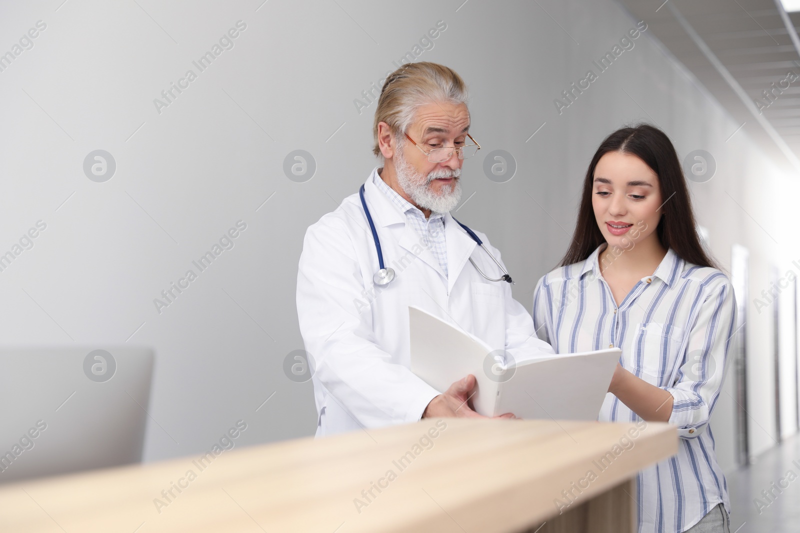 Photo of Senior doctor with notebook consulting patient in clinic