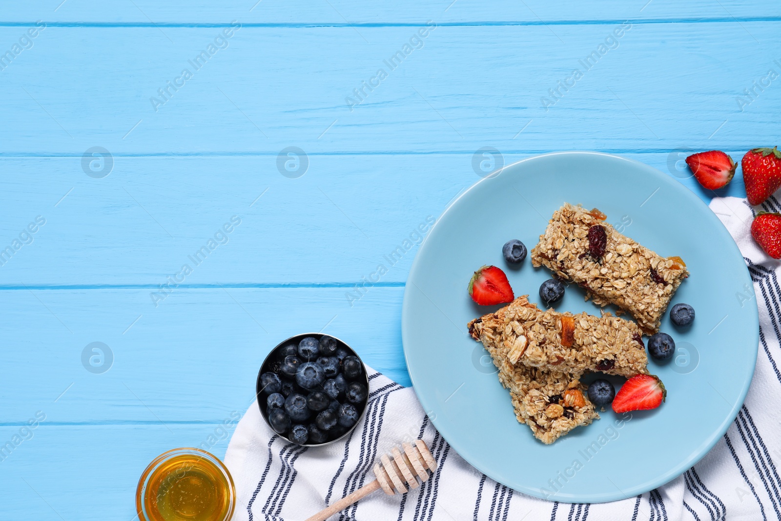 Photo of Tasty granola bars with berries and honey on light blue wooden table, flat lay. Space for text