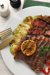 Photo of Delicious grilled beef steak and vegetables served on light wooden table, top view