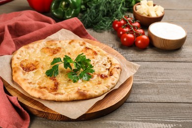 Photo of Delicious khachapuri with cheese, parsley and vegetables on wooden table