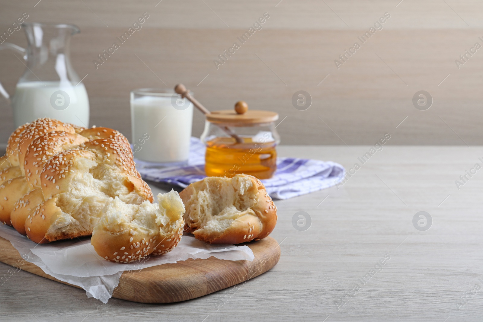 Photo of Broken homemade braided bread with sesame seeds on wooden table, space for text. Traditional Shabbat challah