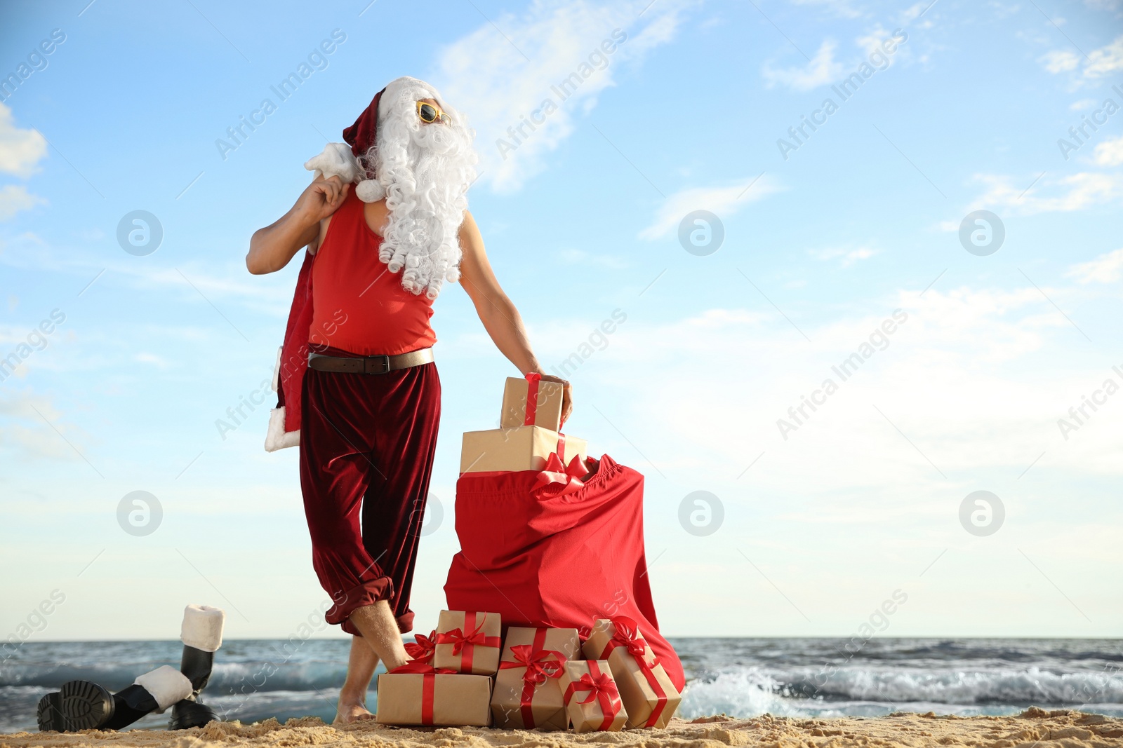 Photo of Santa Claus with bag of presents on beach, space for text. Christmas vacation