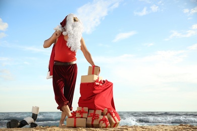 Photo of Santa Claus with bag of presents on beach, space for text. Christmas vacation