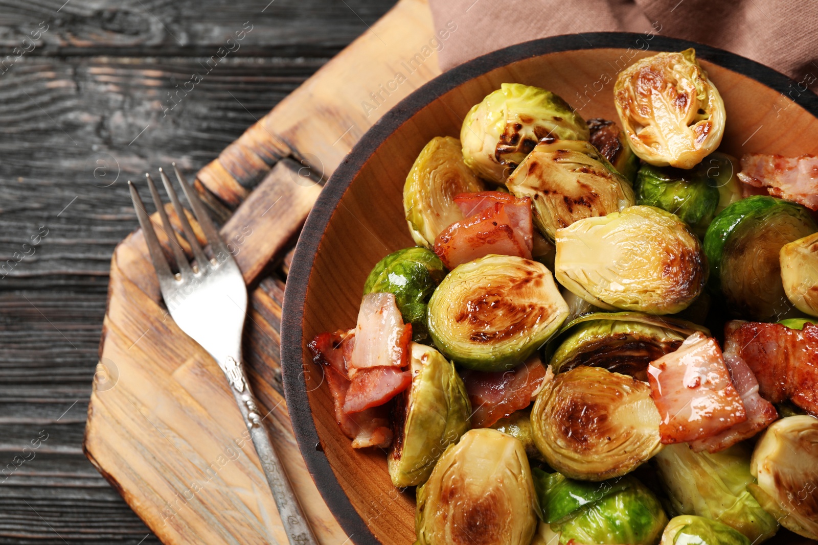 Photo of Delicious Brussels sprouts with bacon in bowl on grey wooden table, closeup