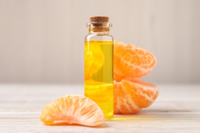 Photo of Bottle of tangerine essential oil and fresh fruit on white wooden table, closeup